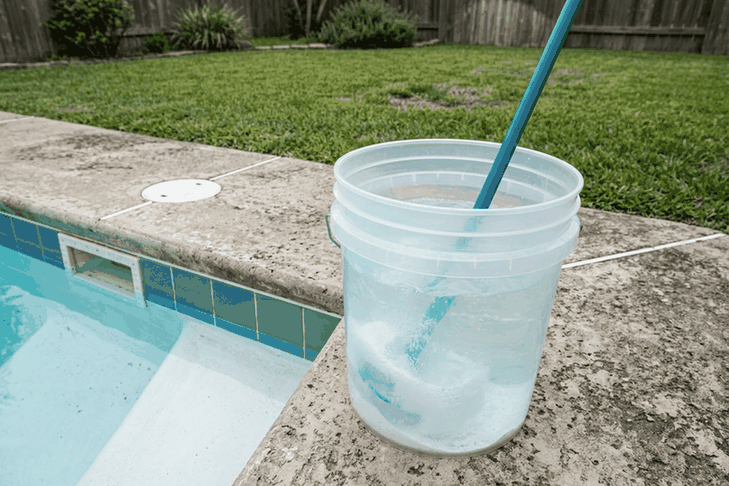 Granular pool shock being stirred into a bucket of pool water on the deck